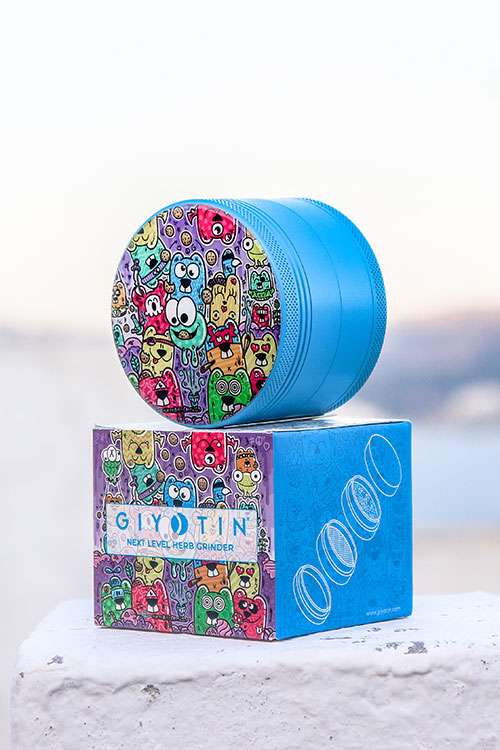 Cookie Timer 4 Piece Ceramic Surface Herb Grinder on standing on Side View on the product packing box. This Weed Grinder comes in Candy Blue with a cool comic design on the top part.